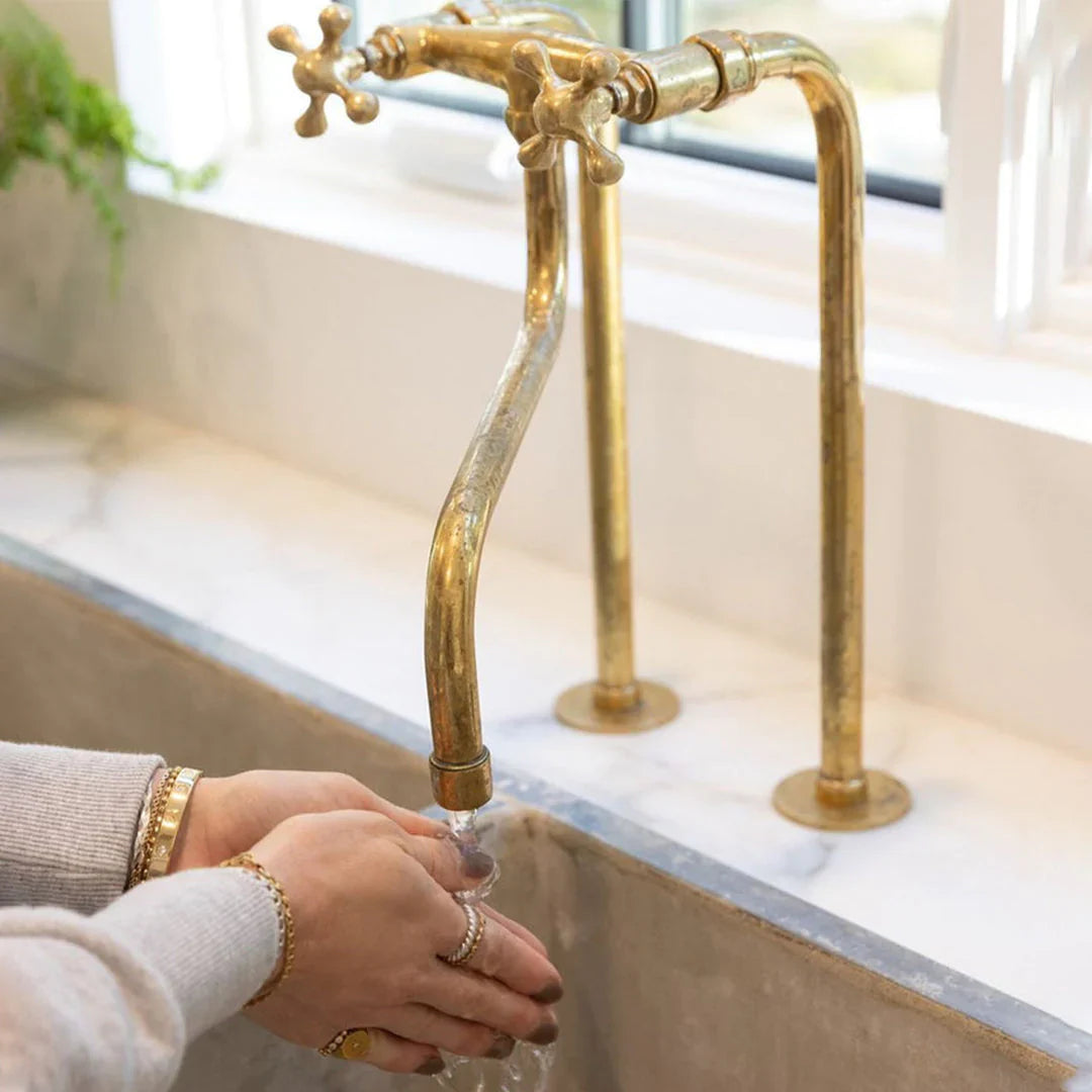 Person washing hands under a gold faucet in a bathroom setting