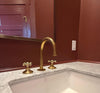 Gold faucet and handles on a marble countertop with a red wall in the background