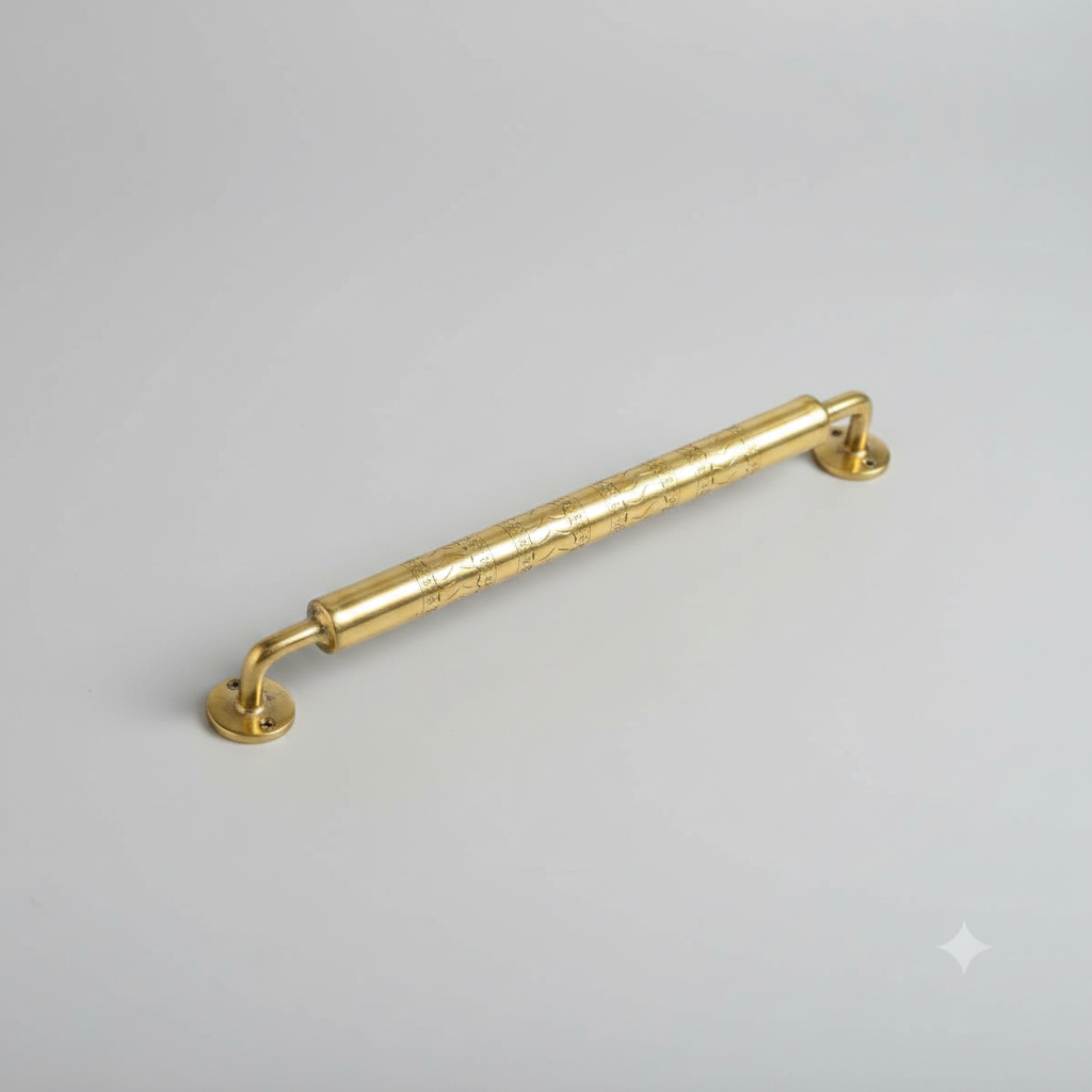 A polished brass cabinet pull handle with engraved floral details, shown resting on a light wood grain surface.