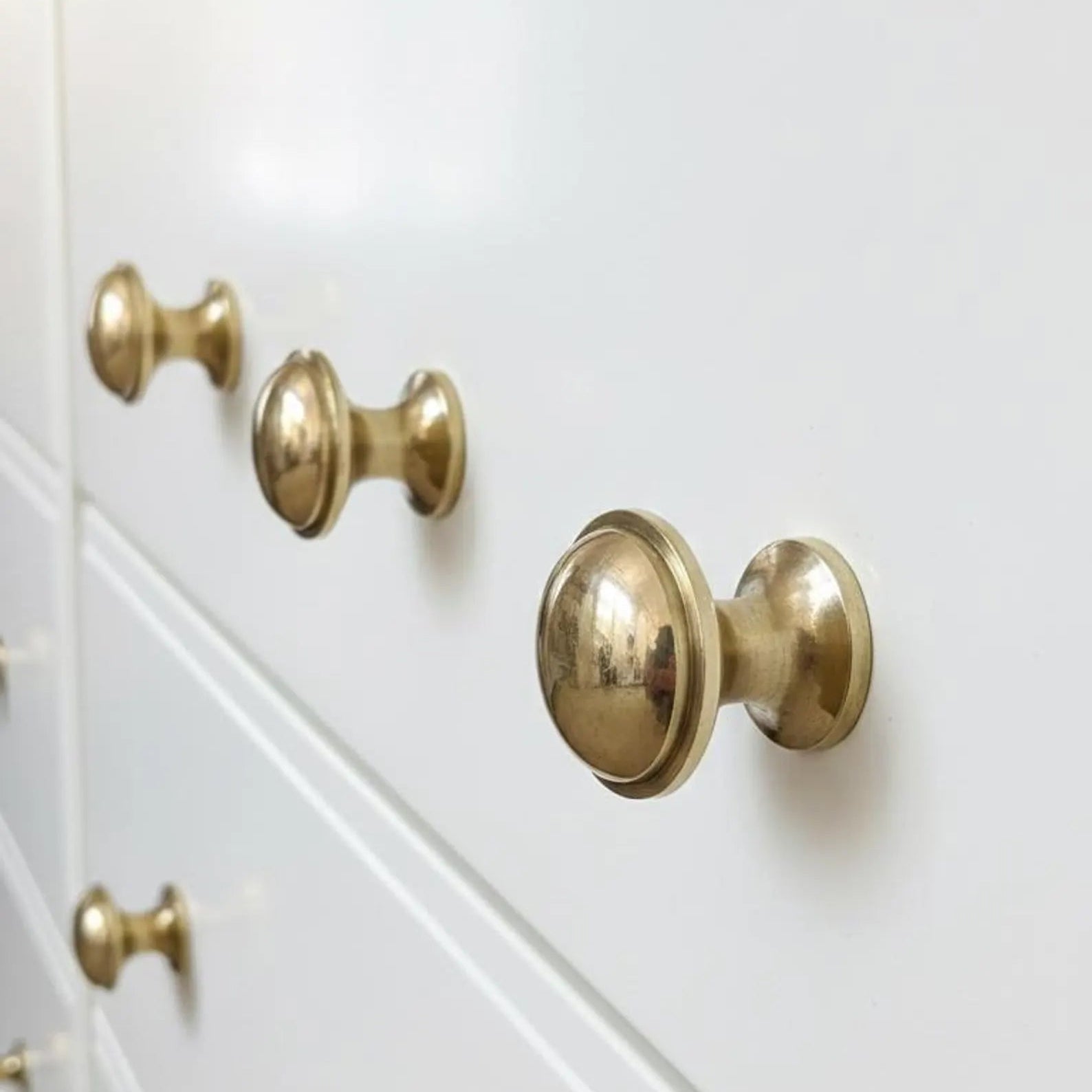 Close-up of a white dresser with polished brass round knobs on the drawer fronts.