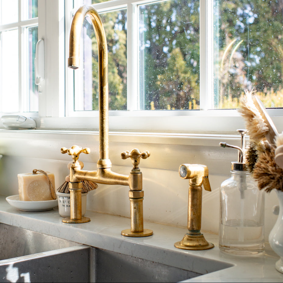 Brass kitchen faucet with a window view of greenery