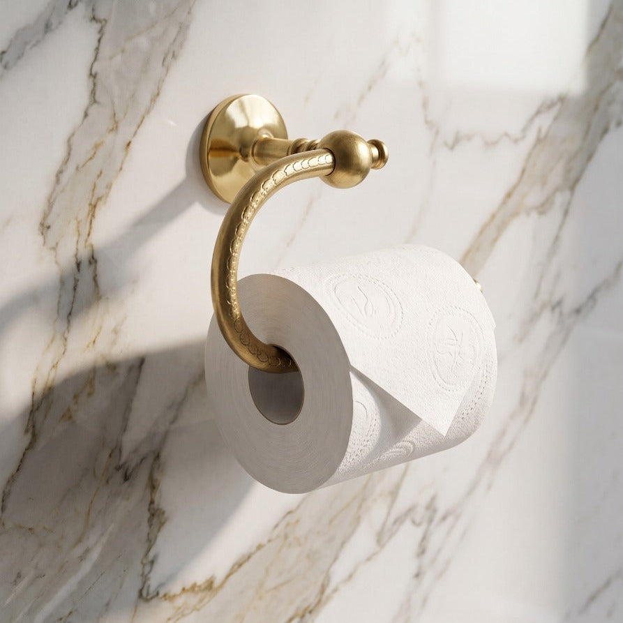 A gold-finished toilet paper holder mounted on a white marble wall with gray veining, holding a white toilet paper roll.