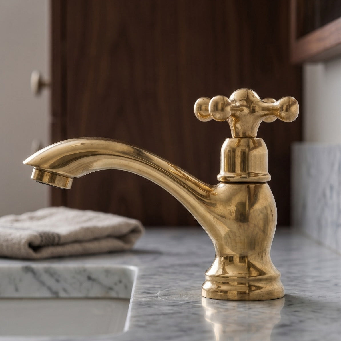 A polished brass single-handle bathroom faucet with a cross-shaped lever, mounted on a gray marble countertop next to a sink.