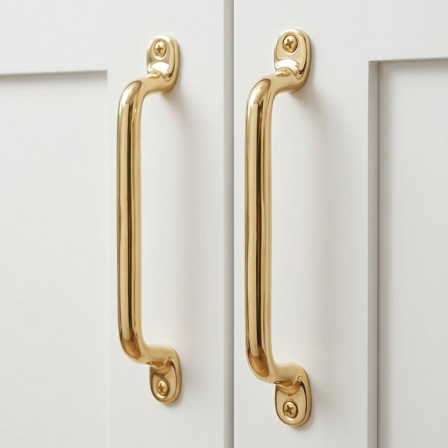 Two polished gold cabinet handles mounted on white shaker-style kitchen cabinets.