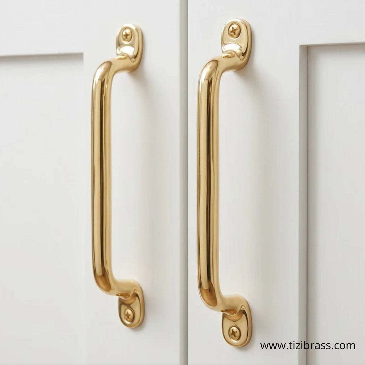 Pair of unlacquered brass cabinet pulls mounted on white cabinet doors